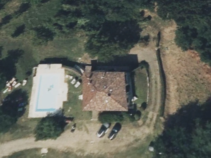 Vista satellitare sfocata di una casa isolata in collina con piscina, circondata da alberi