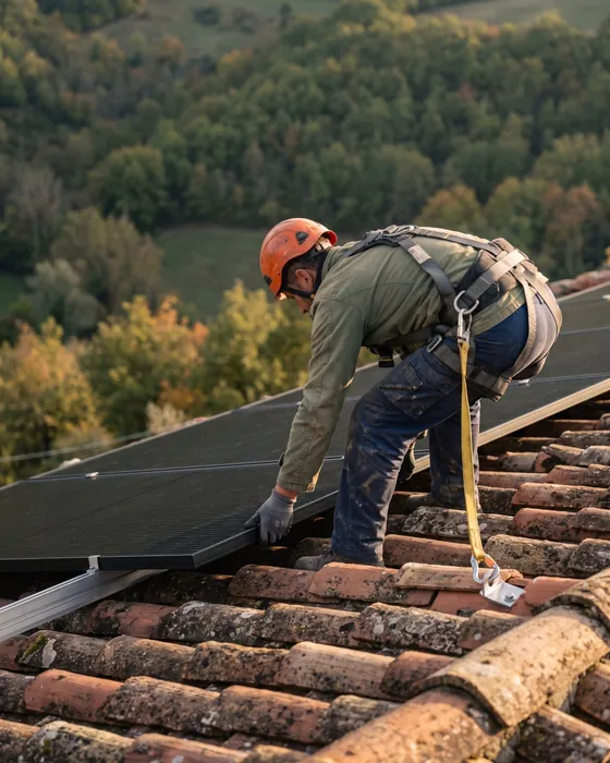 Tecnico al lavoro su un tetto in coppi di una casa di collina, con imbracatura e cordino di sicurezza